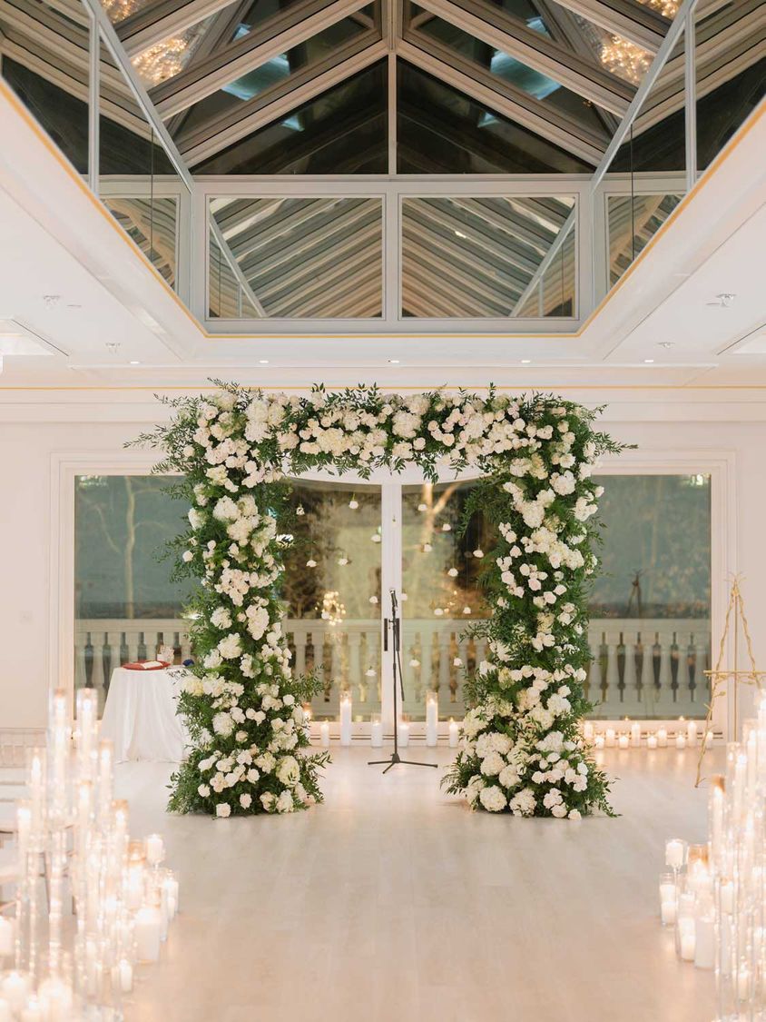 Ceremony arch of white roses and greenery framed by candles
