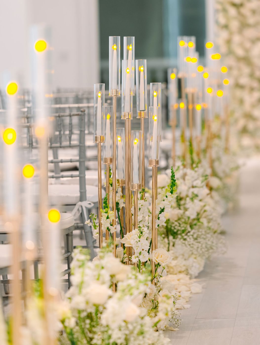 Tall glass candle columns and white flowers lining a ceremony aisle