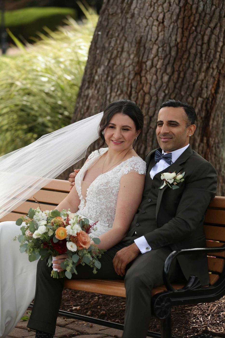 Bride and groom seated on a garden bench under a tree