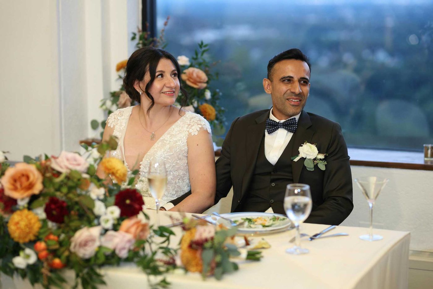Bride and groom at their sweetheart table behind autumn flowers