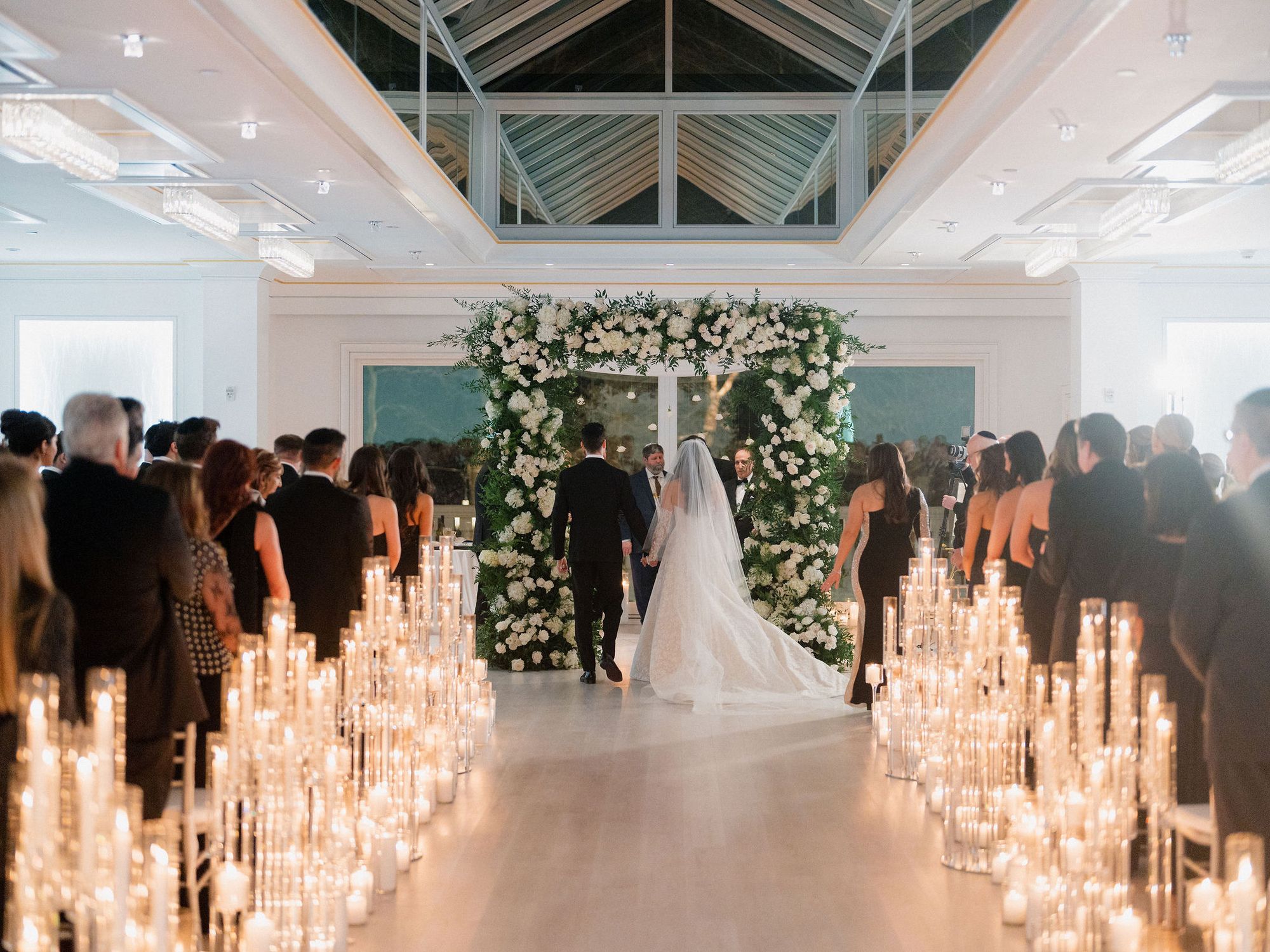 Wedding ceremony under a glass roof with an aisle lined by pillar candles