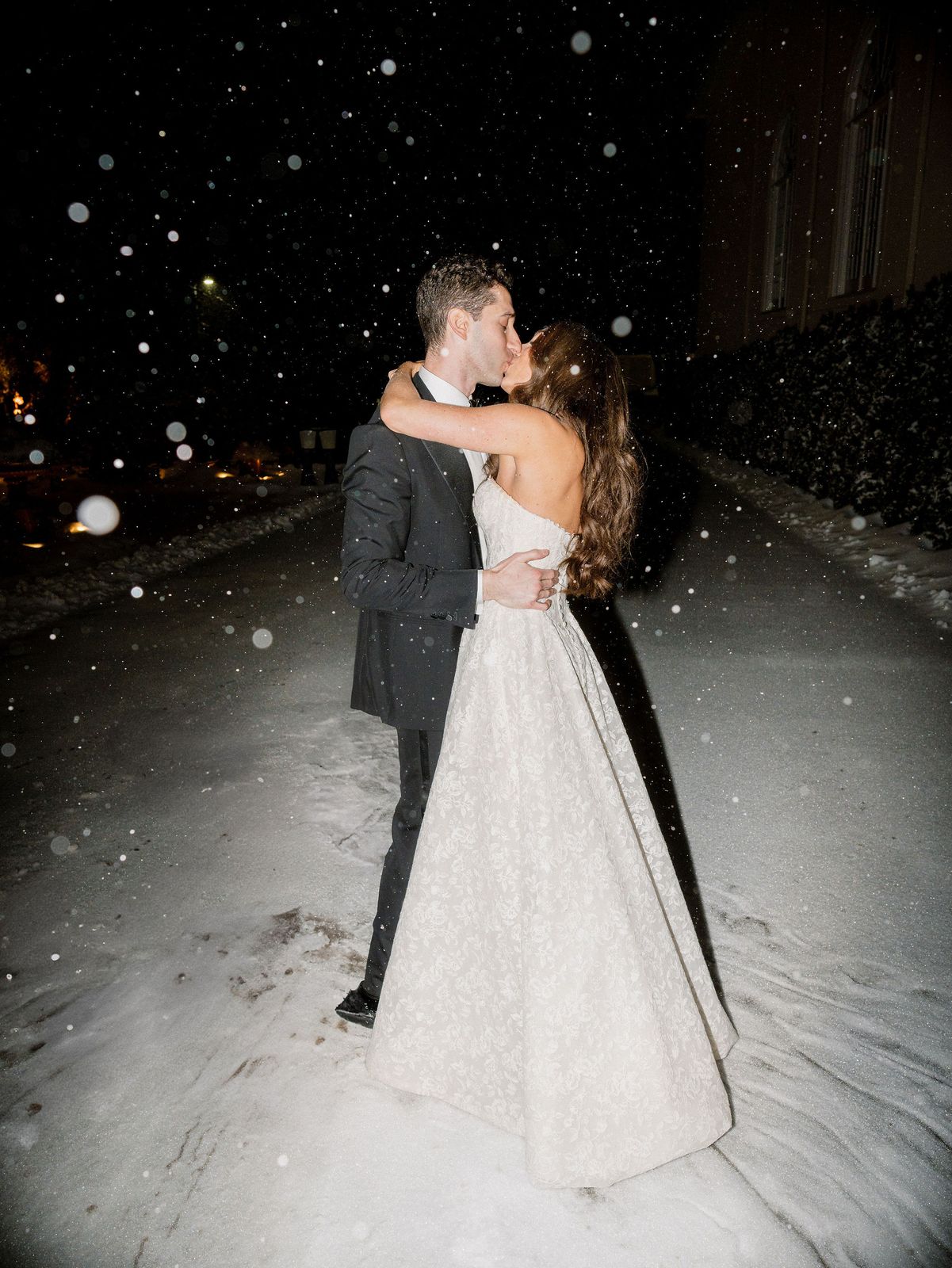 Bride and groom kissing at night as snow falls
