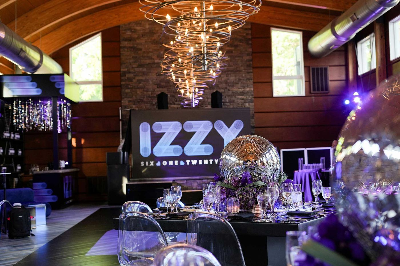 Bat mitzvah dinner tables under a sculptural chandelier with an illuminated name sign