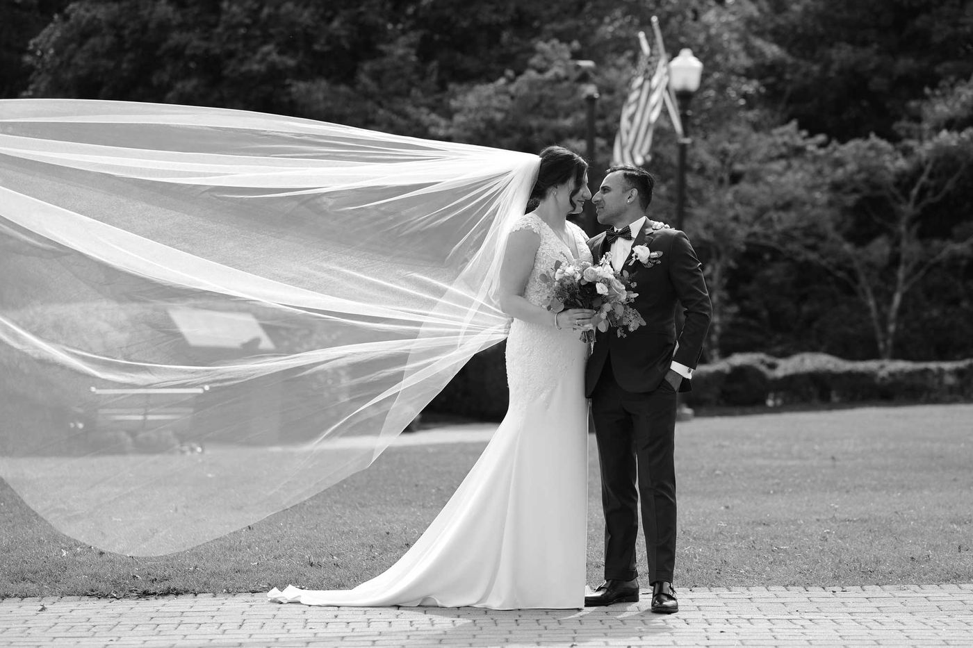 Black and white photo of a couple, her long veil lifted by the wind