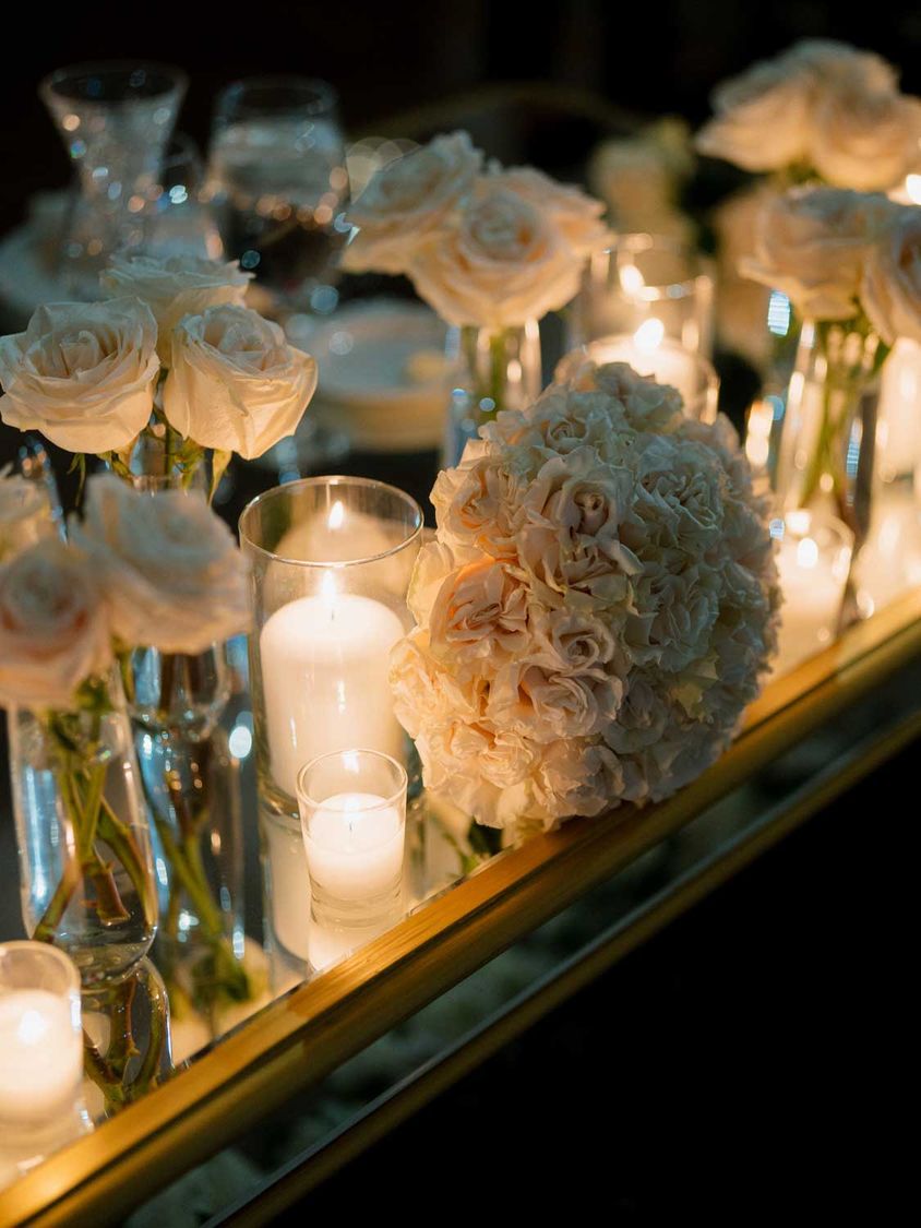 White roses and pillar candles reflected in a mirrored table