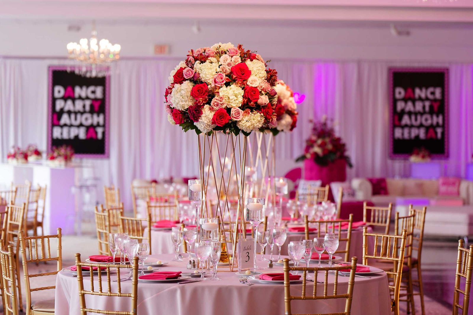 Bat mitzvah reception with tall red and pink centerpieces under pink light