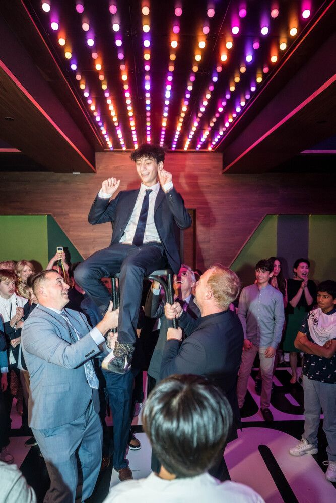 Bar mitzvah boy lifted on a chair during the hora under a ceiling of lights