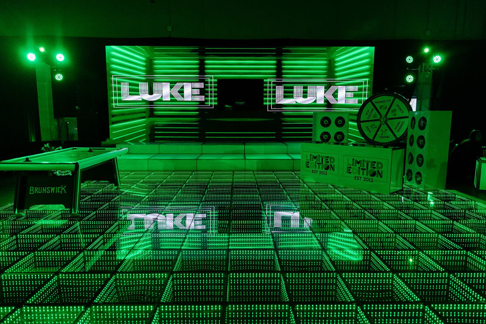 Bar mitzvah dance floor glowing green under LED screens that spell the guest of honor's name