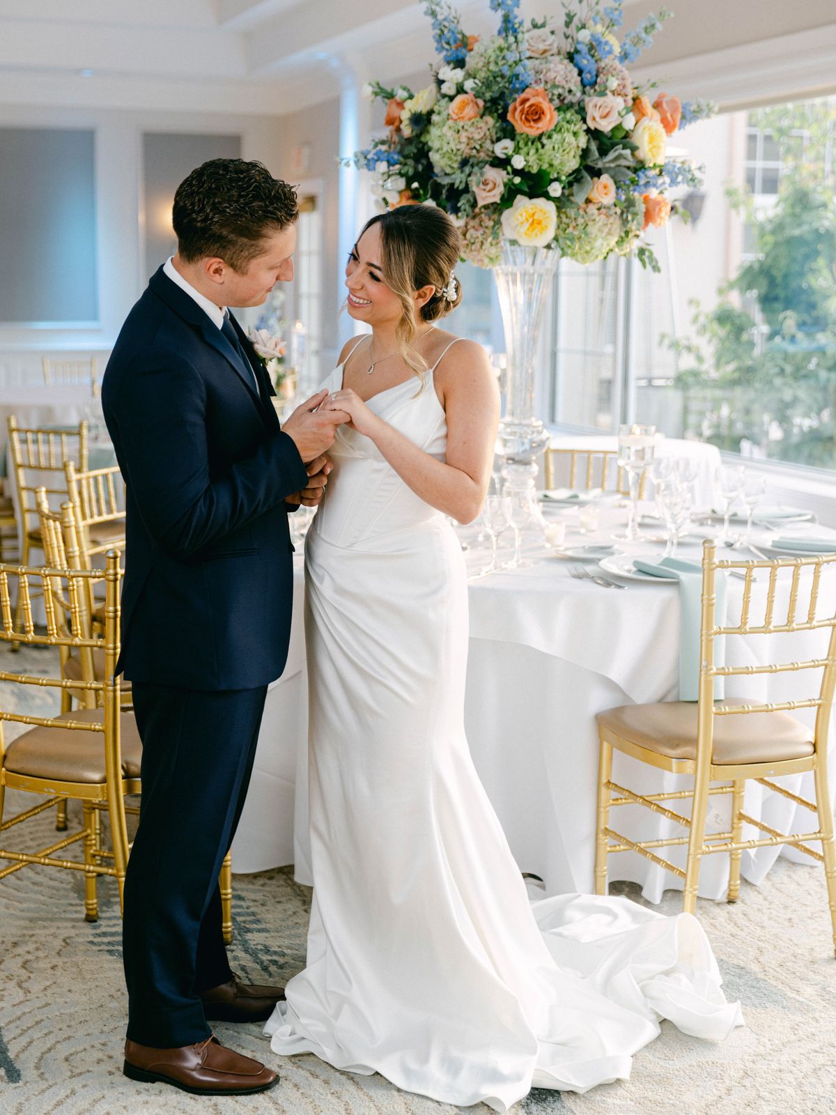 Couple holding hands beside a reception table set with gold chairs
