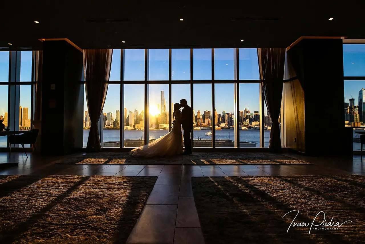 Couple silhouetted against tall windows with the Manhattan skyline at sunset