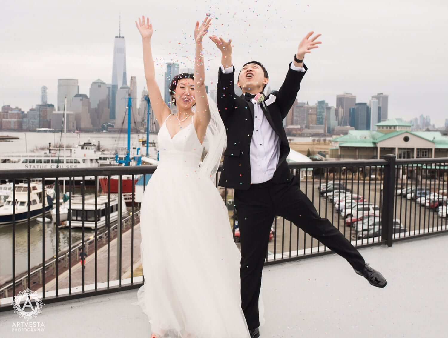 Bride and groom leaping and throwing confetti with the Lower Manhattan skyline behind them