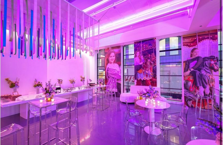 Room in pink and purple light with hanging crystal strands and tall tables