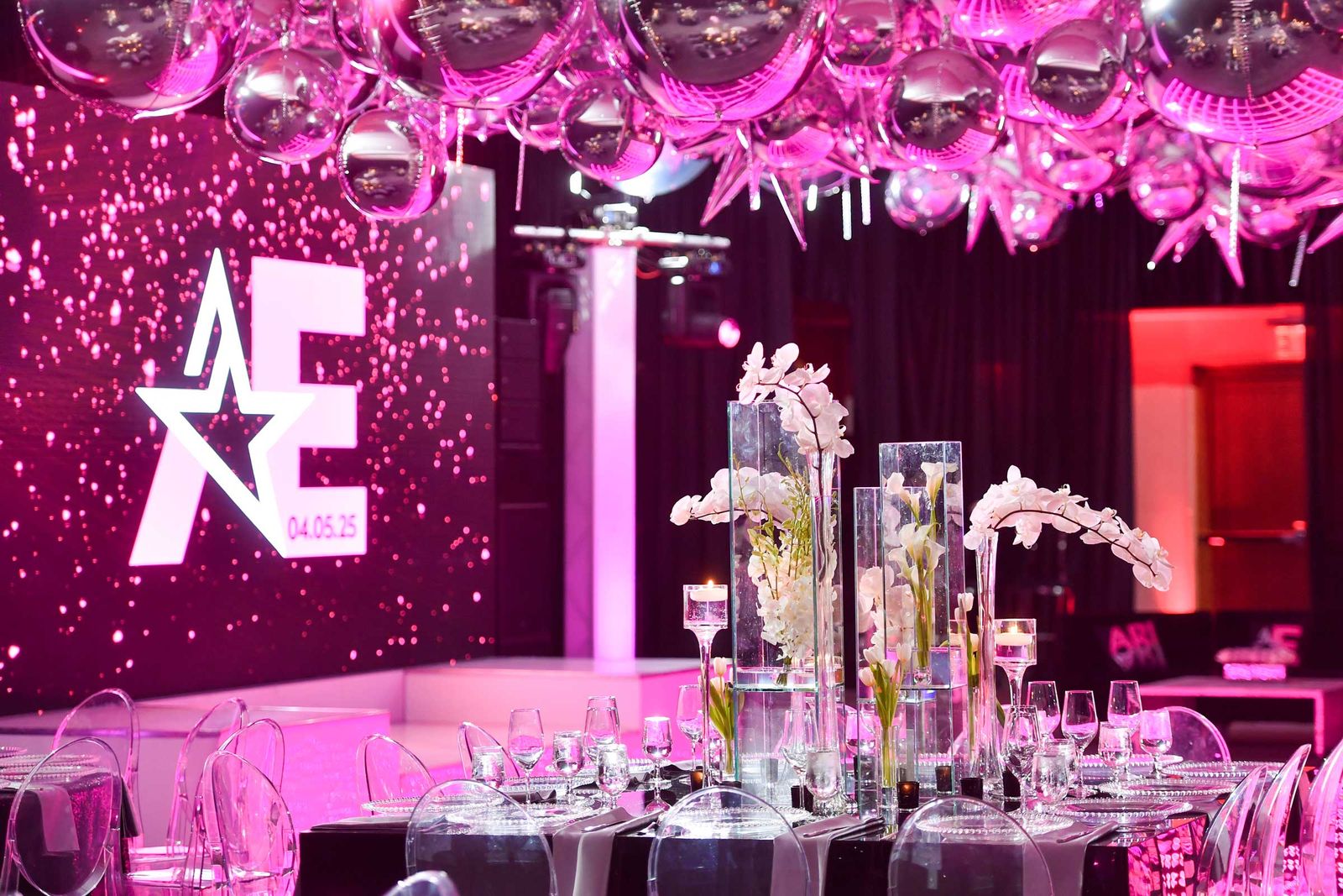 Bat mitzvah tables of white orchids in front of a glowing star logo