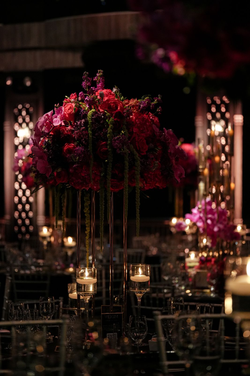 Tall arrangement of red and pink roses on gold stands above candlelit gala tables