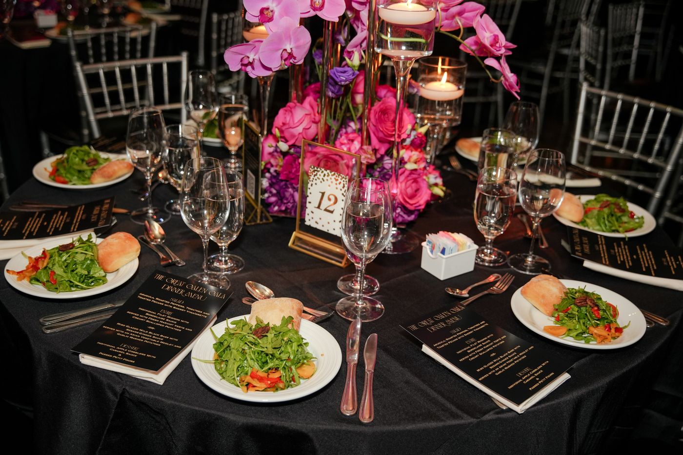 Gala table with pink orchids, floating candles, a gold table number and menus at each seat