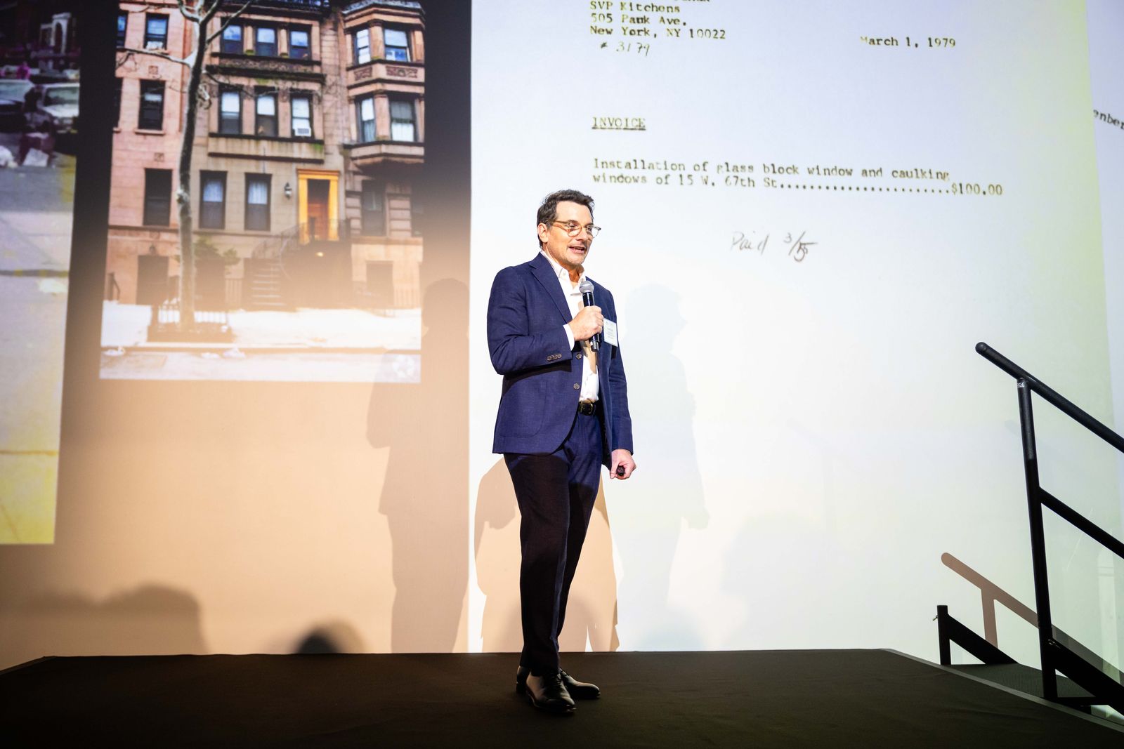 Speaker on stage in front of a projected brownstone photo and a vintage typed invoice