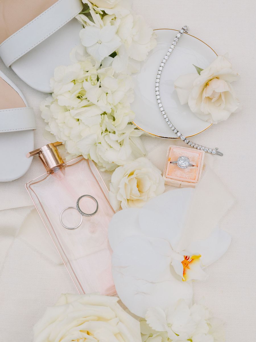 Flat lay of white roses, perfume and wedding rings