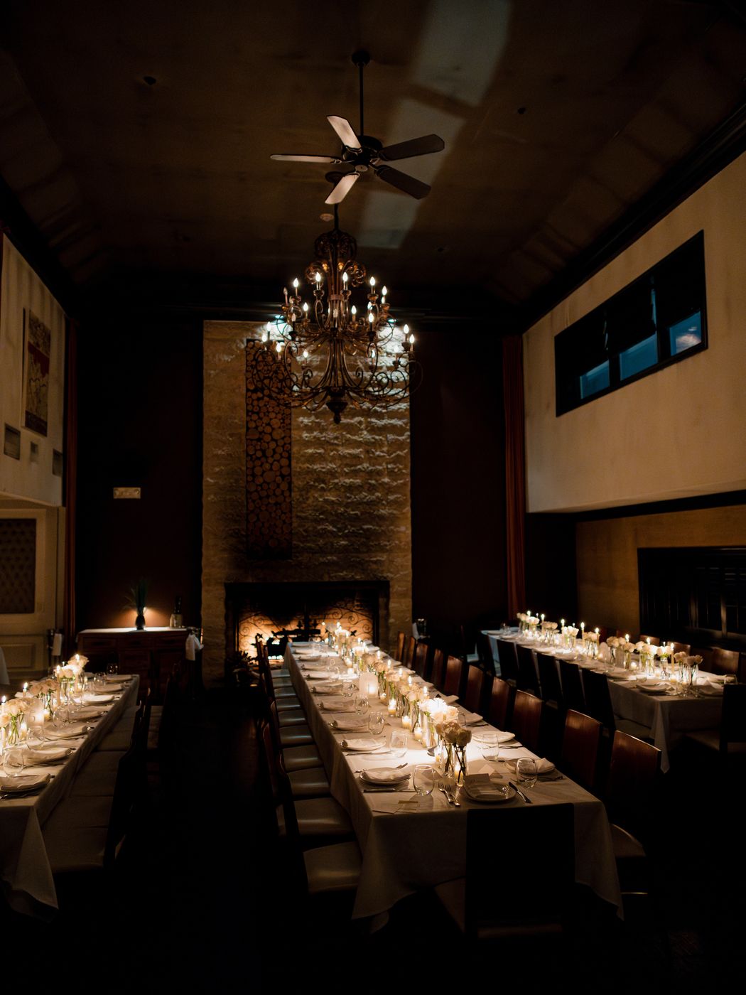 Candlelit rehearsal dinner table with white roses in a dark wood-paneled room