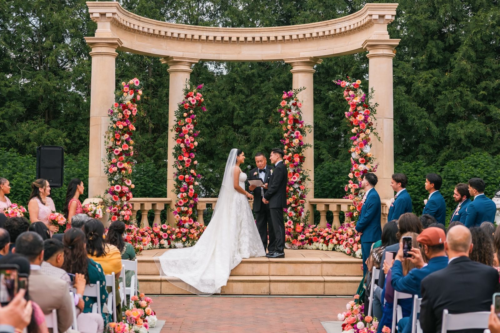 Wedding ceremony under a stone colonnade wrapped in pink and coral flowers